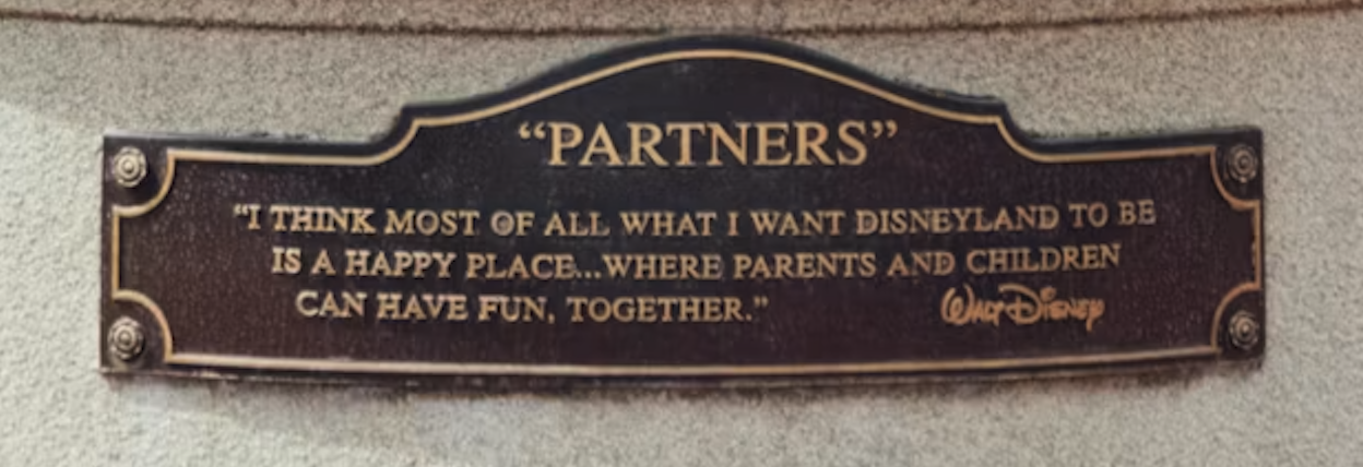 Plaque beneath the Partners statue describing Disneyland as a happy place where parents and children can have fun together